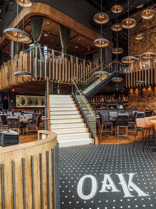 Modern interior of Oak Steakhouse at The Westin Nashville featuring a grand staircase, warm wood finishes, dramatic pendant lighting, and upscale dining spaces.